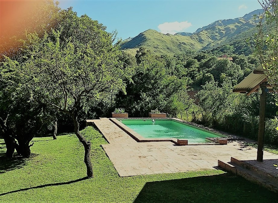 A spacious outdoor area features a well-maintained swimming pool surrounded by a lush green landscape. Mature trees provide shade within the grassy yard, while the backdrop showcases the rolling hills of the sierra. The peaceful setting accentuates the natural beauty of the location.