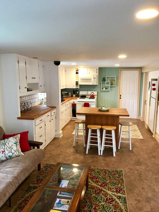 View from private entry door into the apartment. Picture shows the living room transitioning into to kitchen with door to bathroom in the far back.