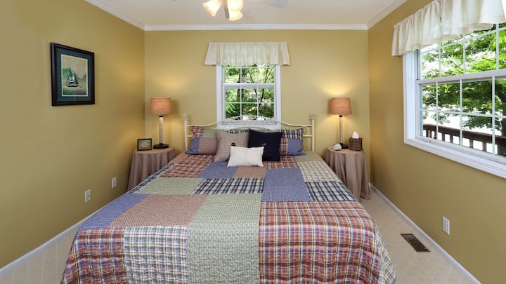 חדר שינה בקומה הראשית עם מיטת קינג סייז, שידות לילה, מאוורר תקרה ונוף לאגם.