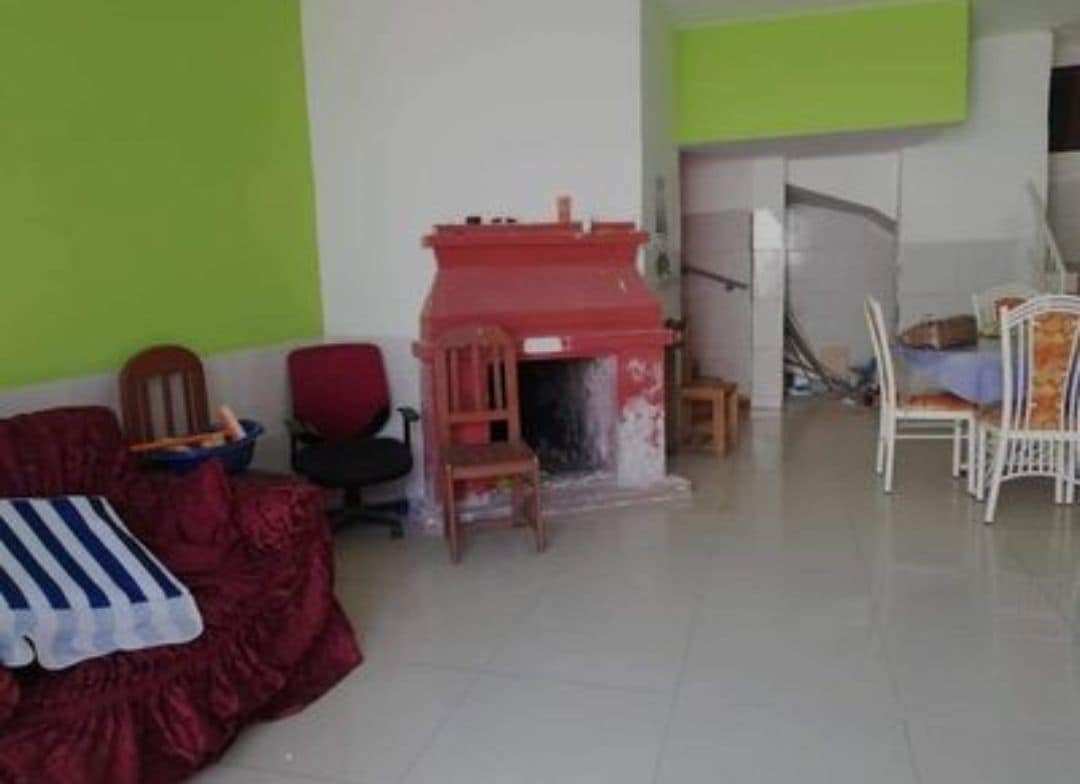 A spacious living area features a traditional fireplace surrounded by seating, including a red couch and chairs. Bright green walls contribute to a lively atmosphere. A dining area with a table and chairs is visible in the background, creating an inviting space for gatherings.