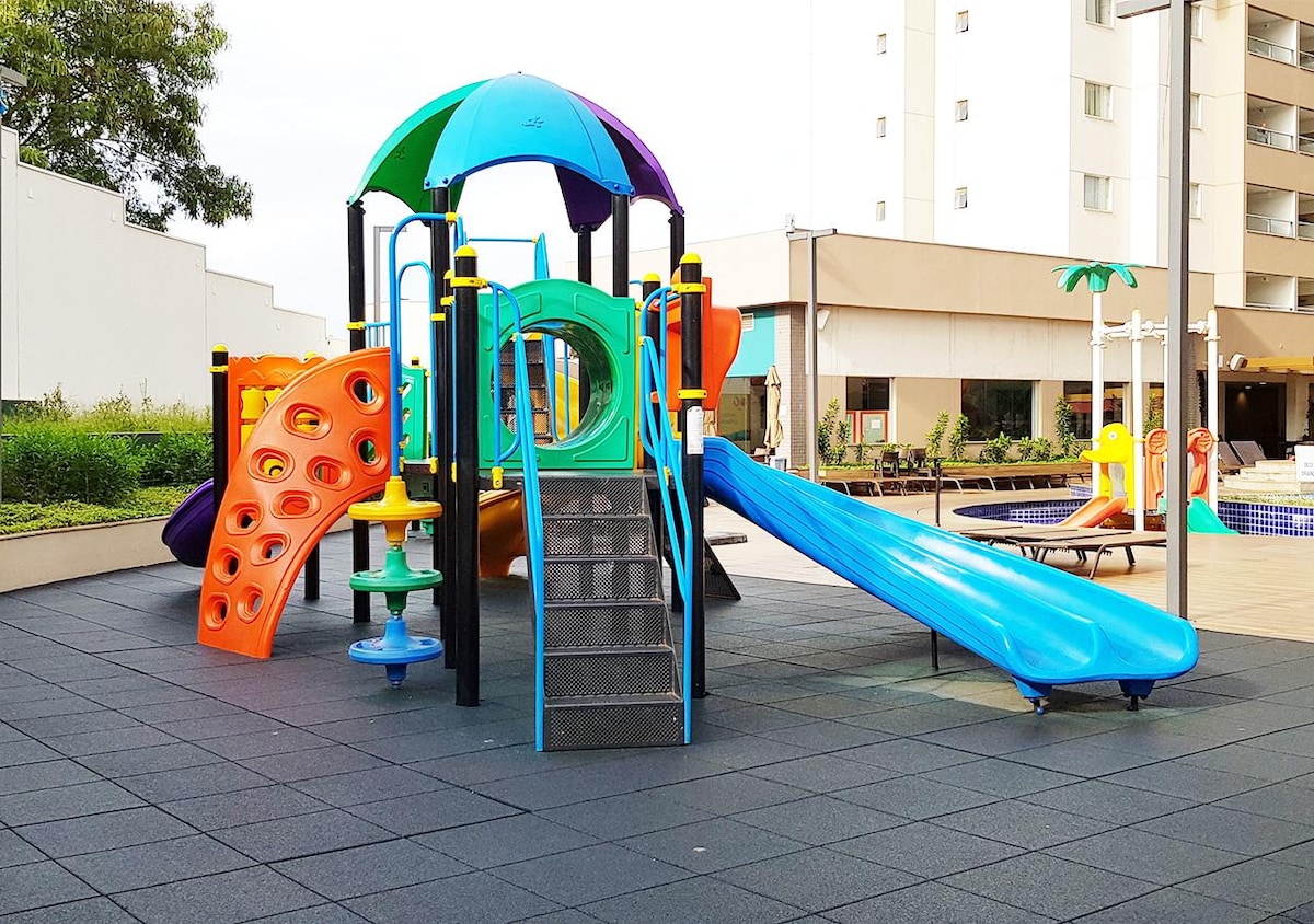 A colorful playground is showcased with features such as slides, climbing structures, and swings. Soft rubber flooring surrounds the play area, ensuring safety. The vibrant equipment is designed for children's enjoyment, making it an inviting space for younger guests.