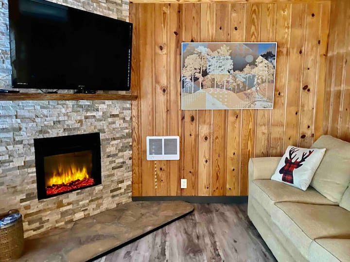 غرفة المعيشة في الطابق الأول، مع سرير أريكة ومدفأة كهربائية وتلفزيون ذكي.