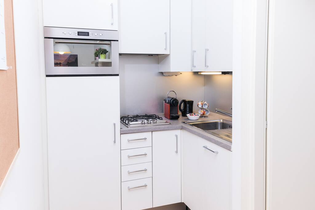 Cucina con macchina per caffè Nespresso, bollitore, forno a microonde, frigorifero, lavastoviglie, freezer e stoviglie per cucinare e pranzare