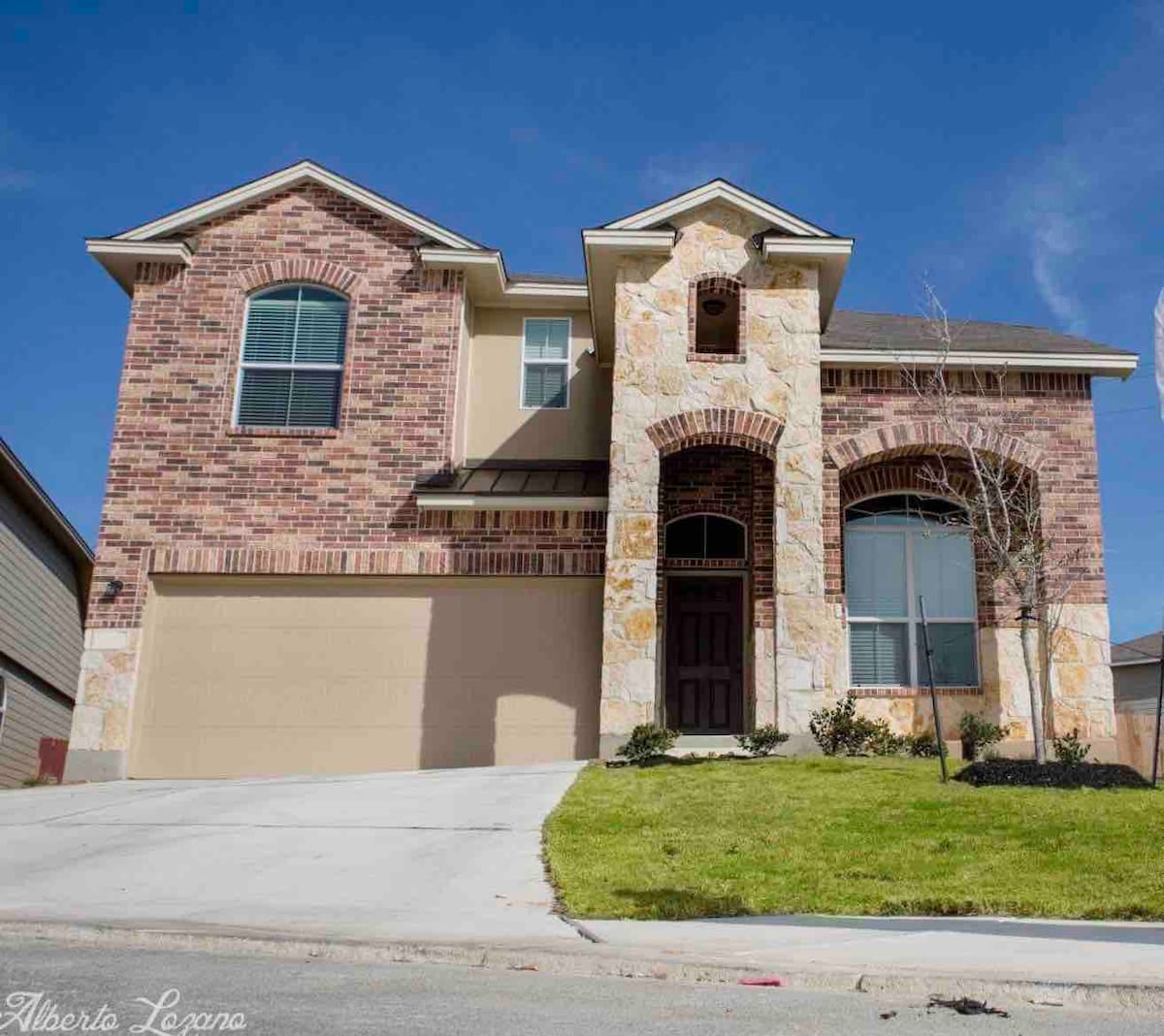 A two-story home features a classic brick and stone façade, with large front-facing windows providing ample natural light. A well-maintained lawn complements the inviting entrance, framed by decorative elements. The driveway leads to a two-car garage, enhancing the spacious exterior appeal.