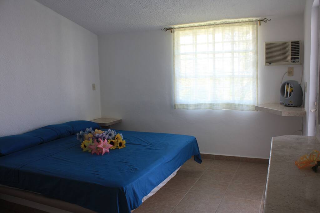 Dormitorio 1 con vista a la alberca, cama King Size, fundas impermeables en almohadas y colchón, aire acondicionado y tocador y buróes laterales de mármol.