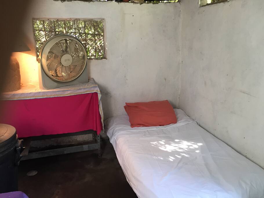 Recámara con sofá cama sencilla mesa metálica con lámpara y ventilador ciclón
