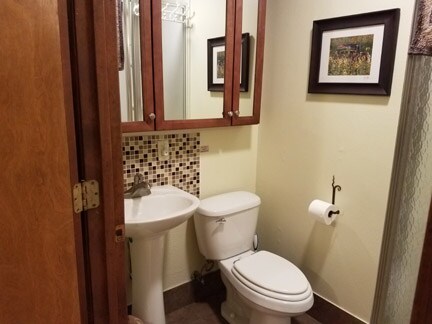 A well-appointed bathroom features a sink with a mirrored cabinet above, providing storage space. A modern toilet is positioned adjacent to the sink, and a roll of toilet paper is mounted on the wall. Decorative tiles are placed behind the sink, adding texture to the space.