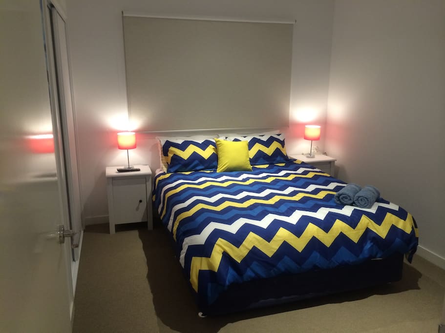 Front view of bedroom. Real queen bed with 4 fluffy pillows. Side table & bedside lamp for each side. Clean towels & linen. (Bedsheet design 1)