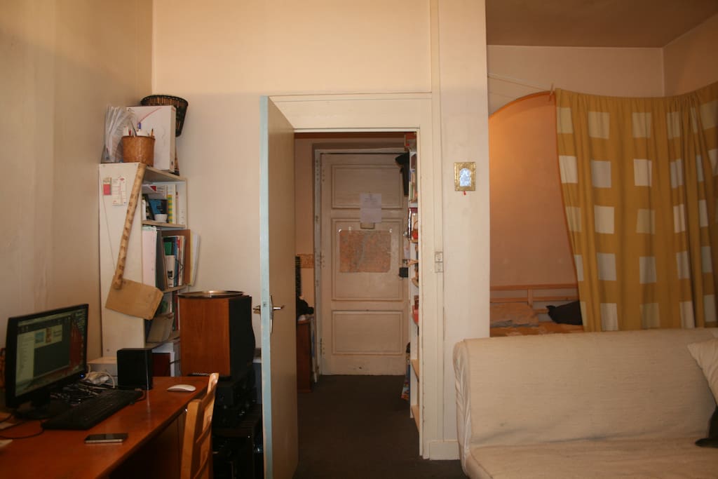 Vue du séjour avec bureau et porte d'entrée à l'arrière-plan.