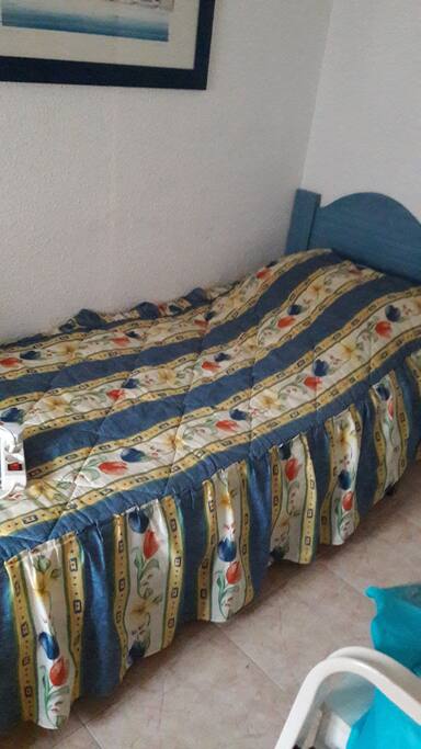 One of two single beds in twin room with wardrobe and side table chest of drawers and mosquito netted window to quiet back of appartment.