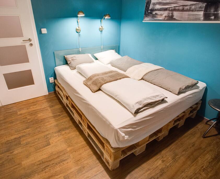Bedroom with a cozy king size palette bed and industrial photographs of Prague and its surrounding.
