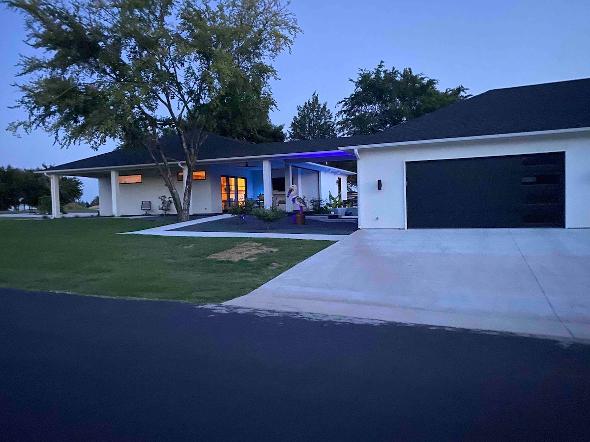 The exterior view showcases a modern garage apartment at dusk, with a well-maintained lawn and landscaping. A spacious driveway is visible, leading to a dark garage door. Soft lighting is emanating from the entrance, highlighting the inviting atmosphere of the home.