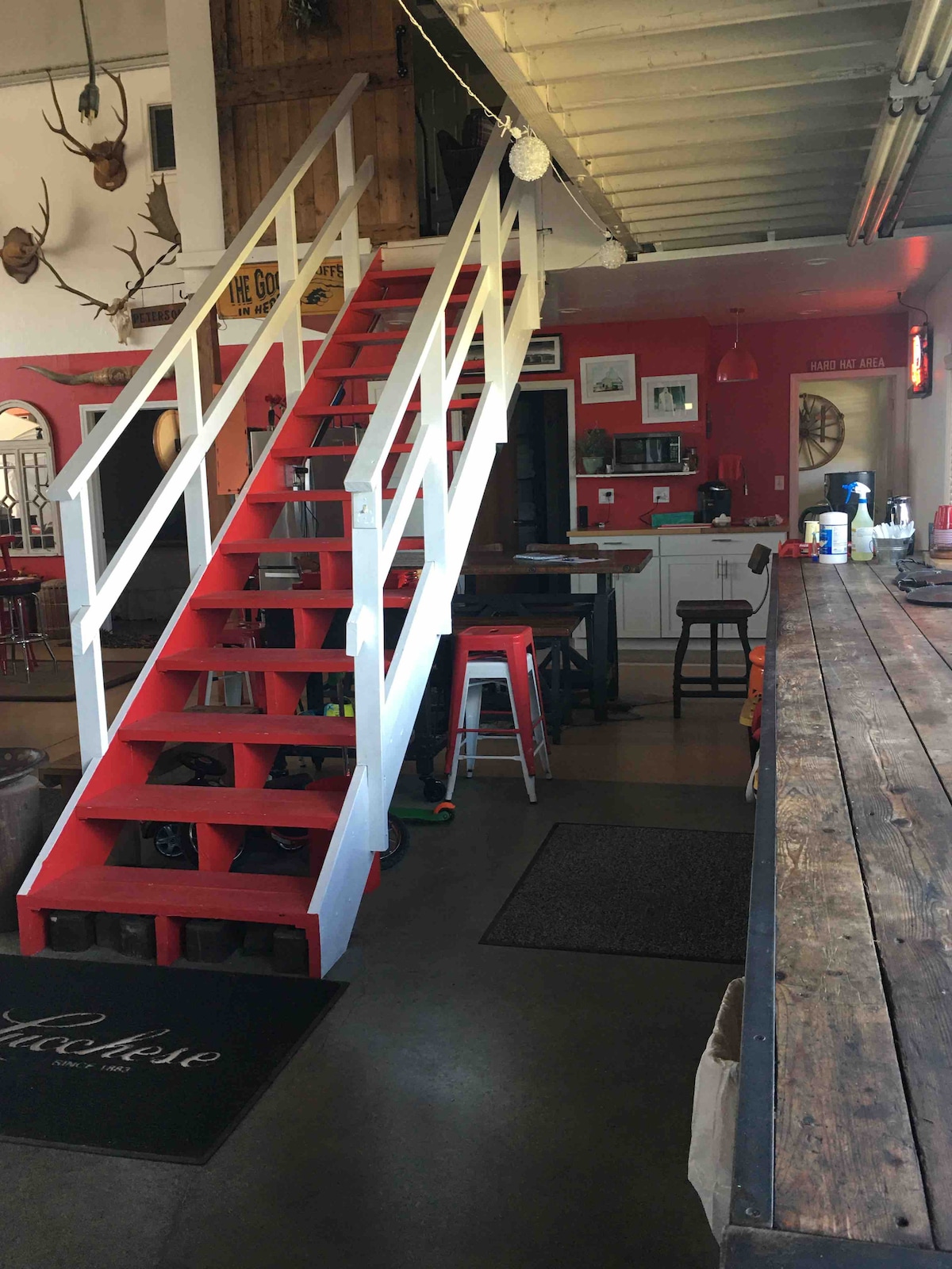 A vibrant interior showcases a red staircase leading to the upper apartment. The open kitchen area includes bar stools and pendant lighting, while a rustic wood counter runs along one side. Decorative elements hint at the building's history, enhancing the inviting atmosphere.