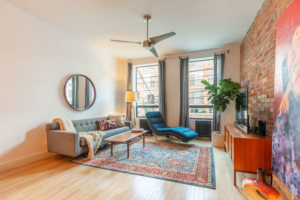 Spacious living room with exposed brick wall, mid-century modern furniture and floor to ceiling windows overlooking Queen West