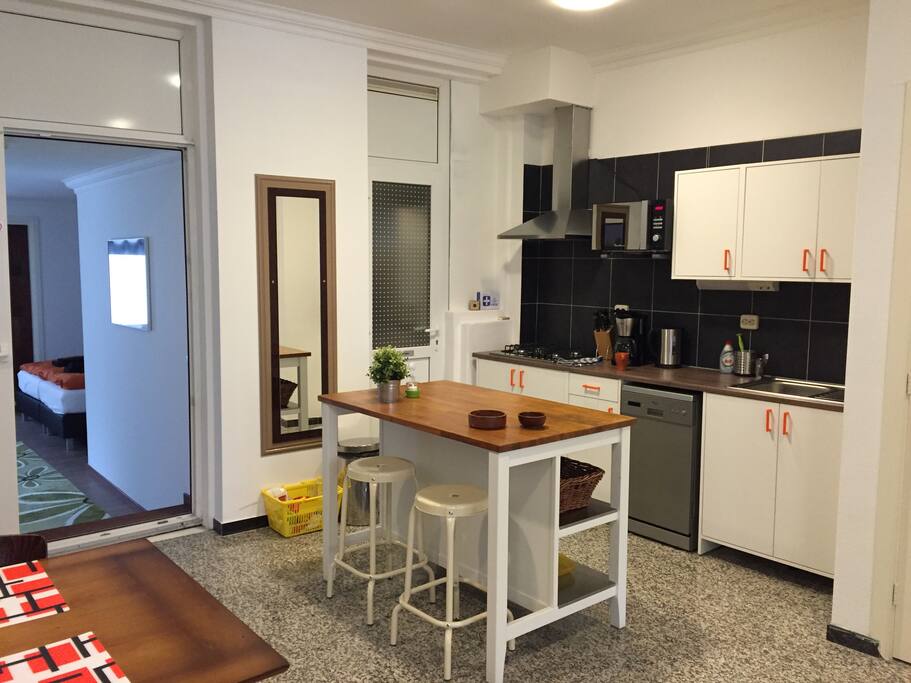 The open kitchen with on the left the entrance of the bedroom, long mirror on the wall and in the right corner the bathroomdoor. The bar table with 2 bar stooles and the kitchencounter with cabinets, the sink, a
4 burner gas stove, dishwasher, cofeemachine, kettle, knife block and the microwave-oven. The kitchen is furnished with cooking utensils, pots and pans, plates,
cutlery, glasses etc. etc., everything you might possibly need!