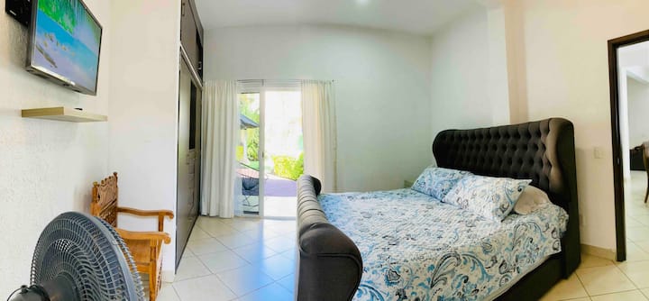 غرفة نوم رئيسية بسرير كبير الحجم وتلفزيون إل جي ومروحة سقف وحمامًا كاملاً. 