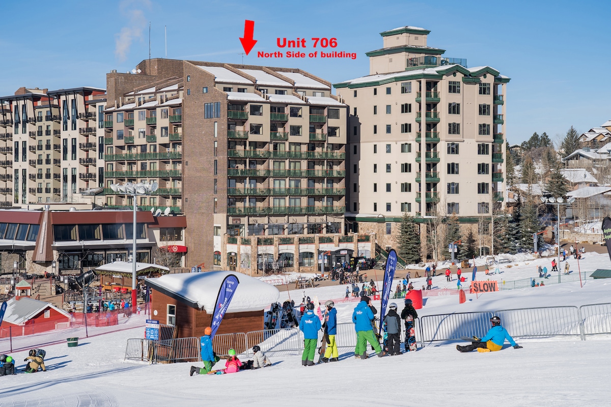 A wide view of the Sheraton Hotel at the base of the Steamboat Ski Area is displayed. The image highlights the unit's location on the north side of the building, with a snowy landscape and skiers in the foreground.