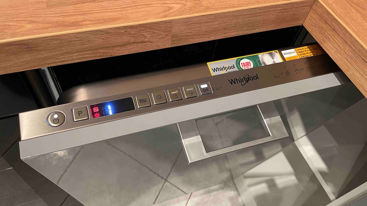 A modern dishwasher is featured under the kitchen counter, showcasing a sleek stainless steel front and intuitive control panel. Buttons are clearly labeled for easy operation, with illuminated indicators for selected settings. The surrounding cabinetry is finished in warm wood tones.