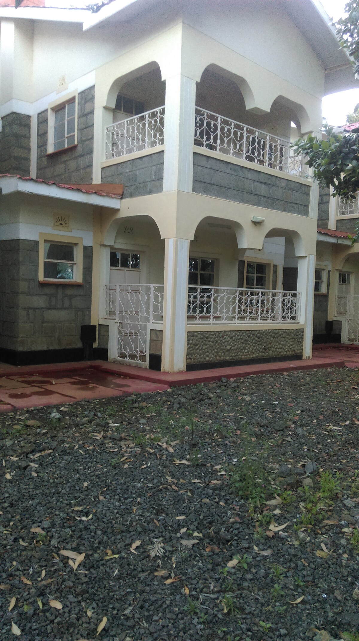 A two-story building features a sturdy stone facade with contrasting light-colored accents. The front entry is framed by arches and includes a decorative balcony with metal railings. Gravel landscaping and a small patch of grass surround the base, providing a well-maintained outdoor area.