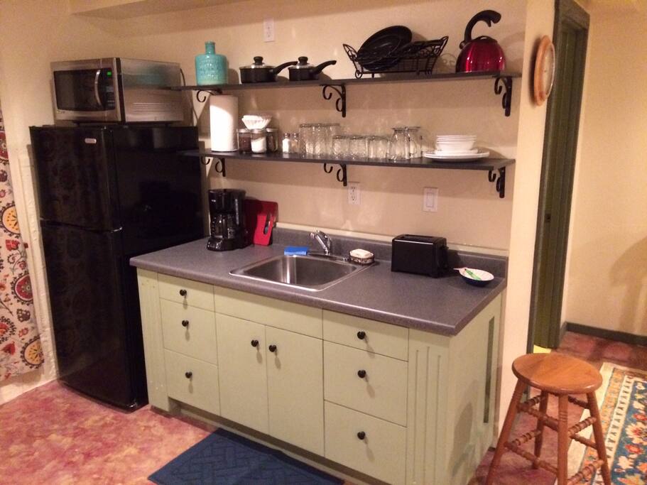 Min-kitchen with fridge, microwave, sink, hot plate, toaster, coffee maker, dishes, and utensils.