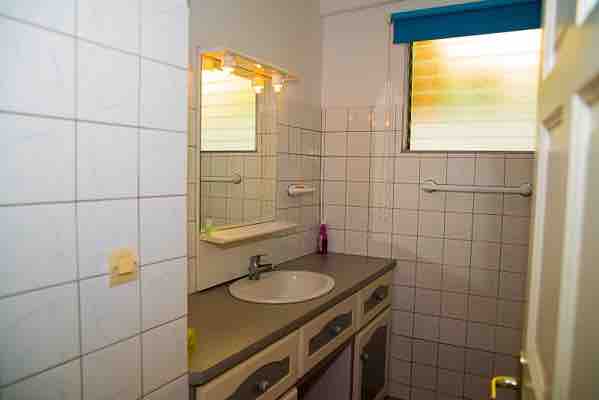 The bathroom features a tiled design with a spacious sink area under a well-lit mirror. A window allows natural light to enter, while a towel rack is mounted on the wall. The overall layout provides a functional space for daily routines.