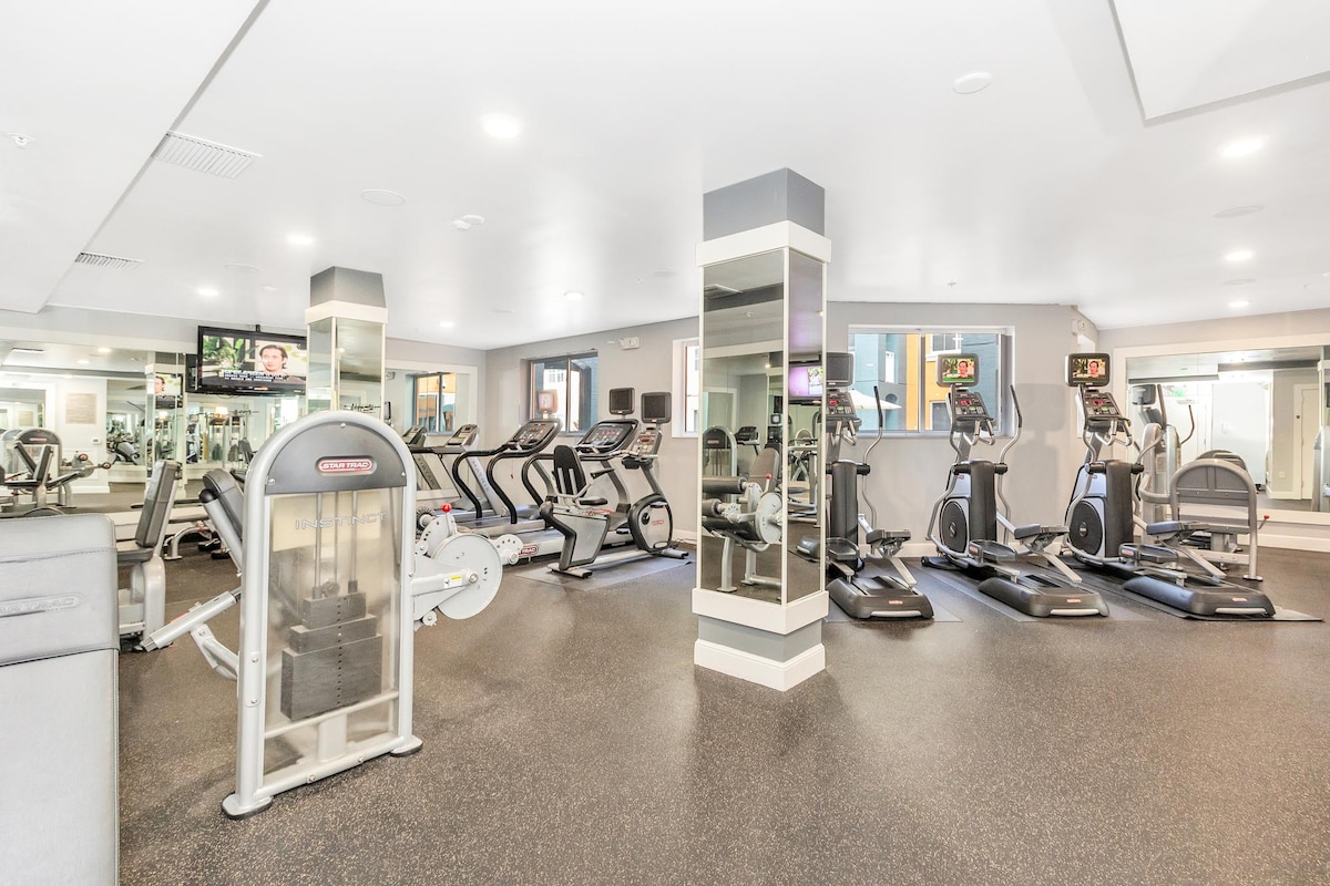 A well-equipped fitness center is showcased, featuring various cardio machines including treadmills and ellipticals. Large mirrors and bright lighting enhance the modern aesthetic. The space is designed with accessible pathways, allowing easy navigation for all guests.