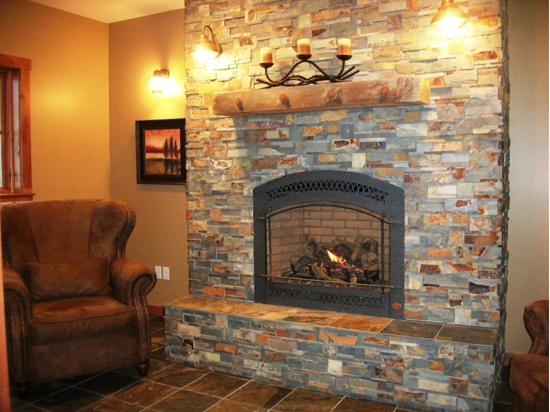 A stone fireplace adorned with candles serves as a cozy focal point in the living area. Two comfortable armchairs are positioned nearby, creating a welcoming atmosphere. Soft lighting enhances the warm tones of the walls and the natural stone texture.