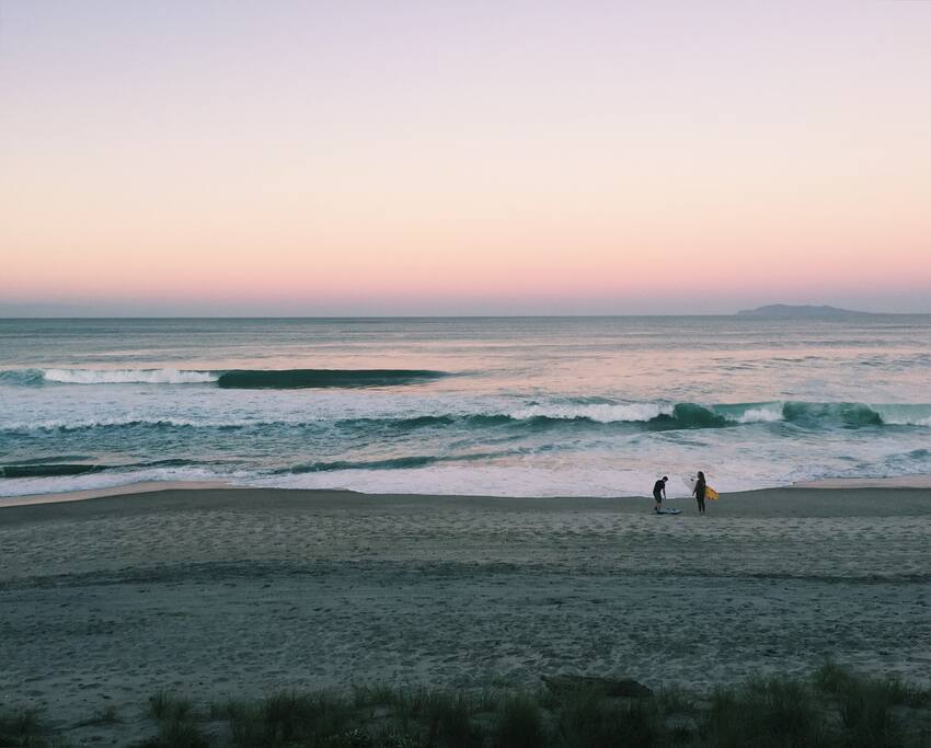 Surfers on Whiritoa Beach at dusk