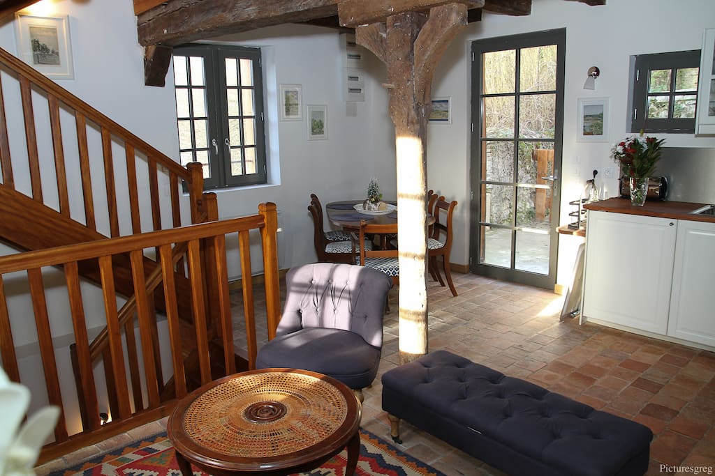 Vue du séjour vers la terrasse. Poutres anciennes apparentes, mobilier ancien, tomettes anciennes, très grande luminosité.