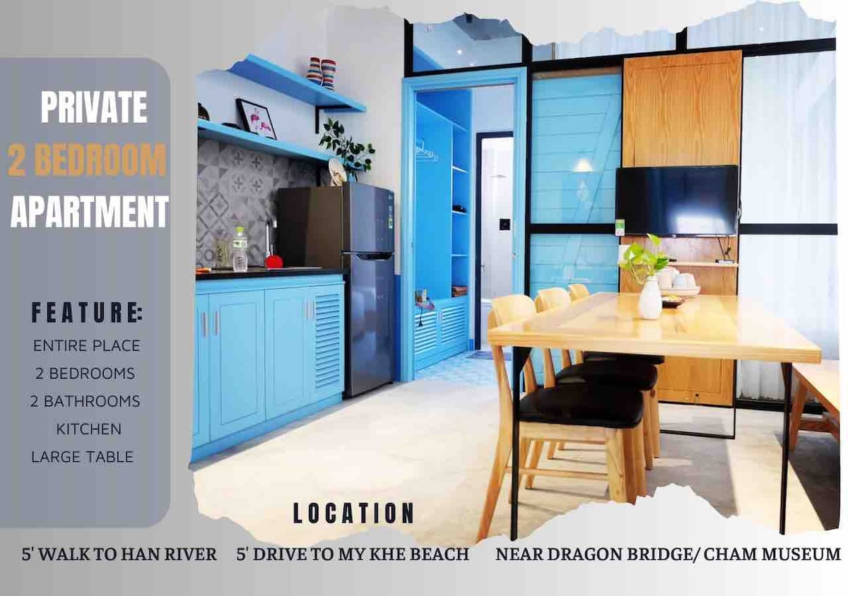 A well-lit kitchen and dining area features a large wooden table surrounded by black chairs. Blue cabinetry provides ample storage. The space is designed for comfort and functionality, with a modern kitchen setup visible in the background.