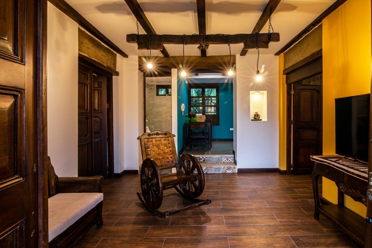 A traditional wooden rocking chair is positioned in the center of the room, complemented by a cozy seating area. The ceiling features exposed wooden beams, while warm light fixtures add a welcoming touch. Doorways lead to other rooms, highlighting the home's open layout.