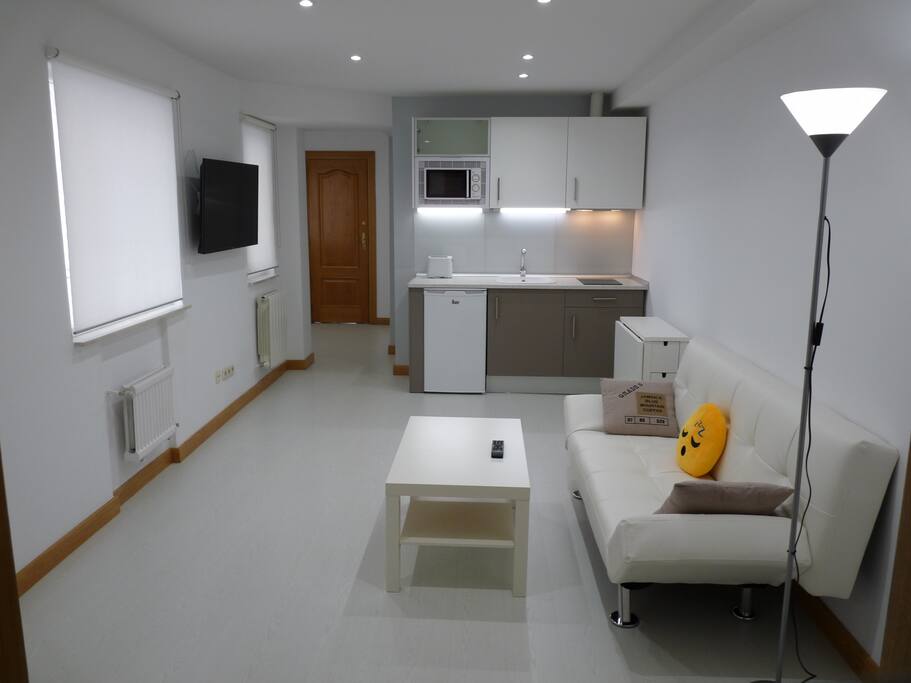 Vista salón con sofá, televisión 43" con WIFI y cocina.