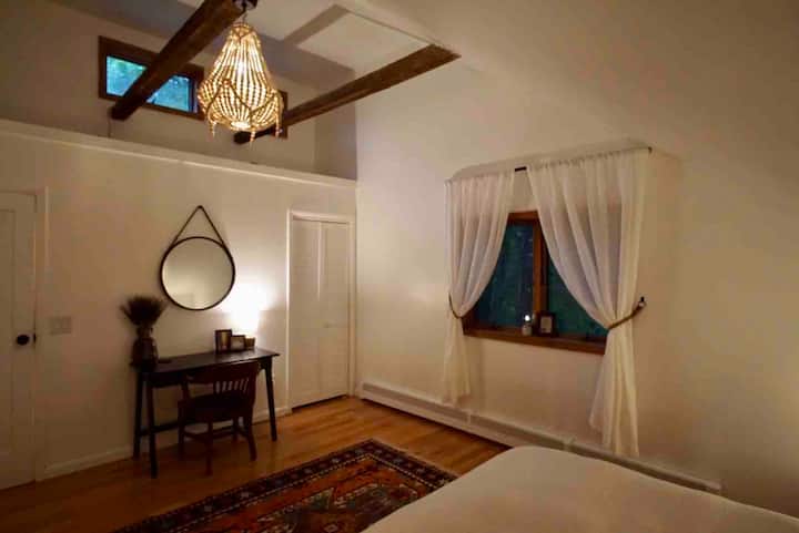 Dhomë gjumi primare me banjë ensuite, krevat dopio "queen" dhe tavolinë.