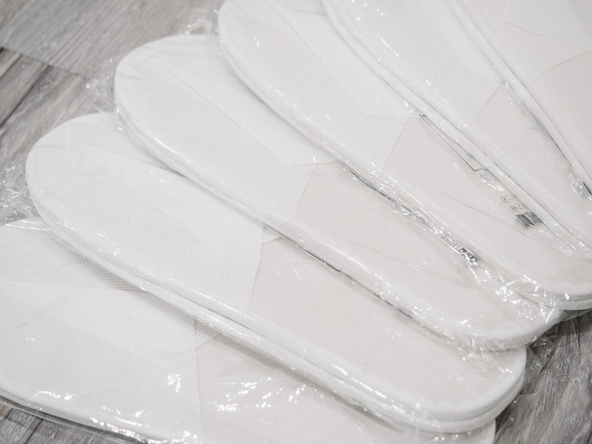 Multiple pairs of white slippers are neatly arranged, each wrapped in clear plastic. The soft, textured material is visible, designed for comfortable indoor use.