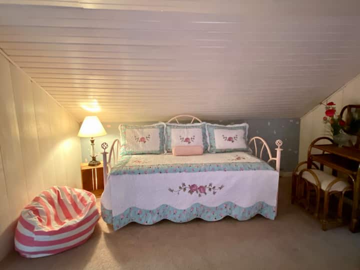 Day bed with pull out trundle, rattan vanity, beanbag seating & side lamp in bedroom with low vaulted ceilings on second floor.