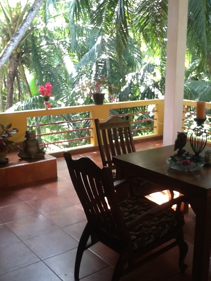 A private terrace is surrounded by lush greenery, featuring a wooden table and two chairs. Decorative elements, such as potted plants and a statue, complement the tranquil setting, creating an inviting space to relax and enjoy nature.