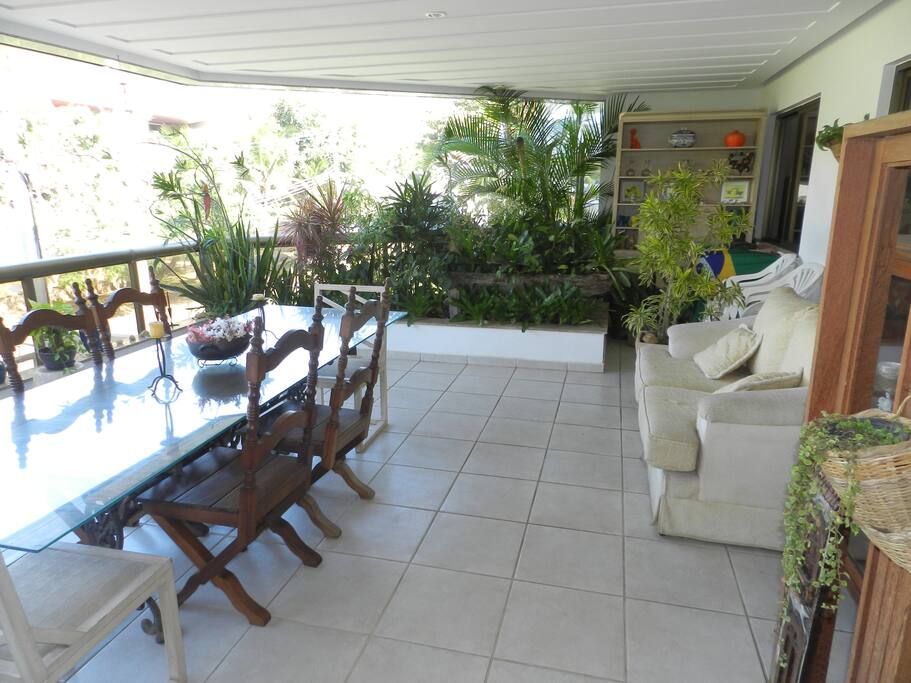 Varanda ampla e confortável, com mesa de jantar, sofá e cadeiras.