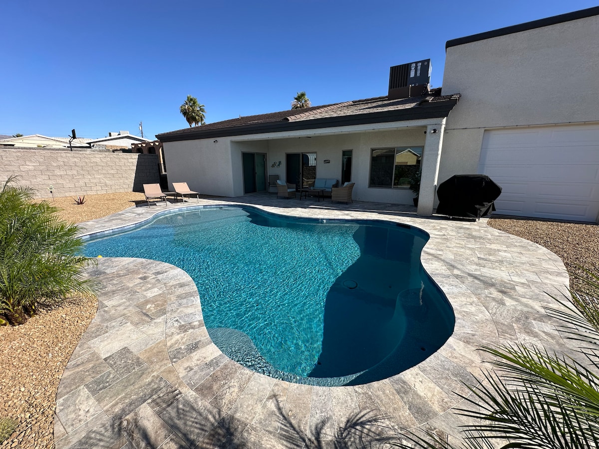 A spacious backyard features a newly installed in-ground pool, surrounded by a stone patio and tropical landscaping. Comfortable lounge chairs are positioned near the pool, providing areas for relaxation. A covered seating area is visible, enhancing the outdoor entertainment space.