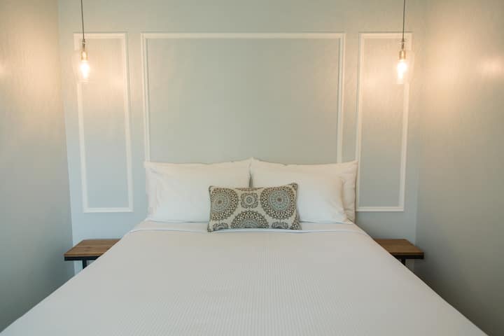 Queen sized bed with luxury linens and four lush pillows with two bed side tables.