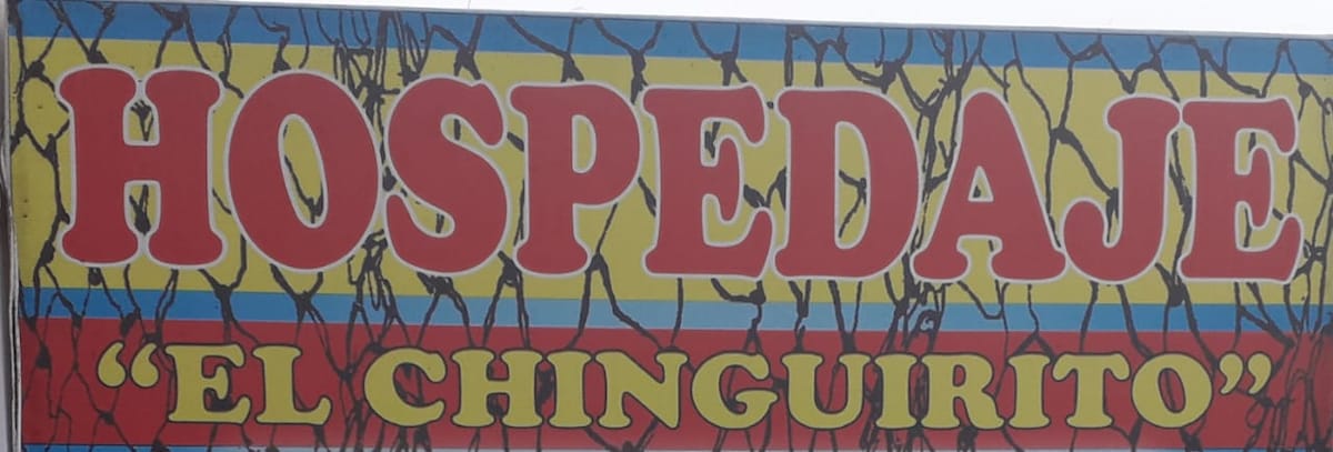 A colorful sign features the name 'HOSPEDAJE' prominently in bold red letters, with 'El Chinguirito' displayed in a smaller, playful font. The background showcases bright yellow and blue stripes, creating a vibrant visual identity.