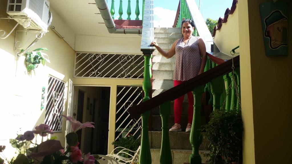 A staircase is featured leading to the upper level, surrounded by vibrant green railings. The area is brightened by natural light, with potted plants adorning the base of the stairs. Two doors open into the interior space, facilitating access to the home's various amenities.