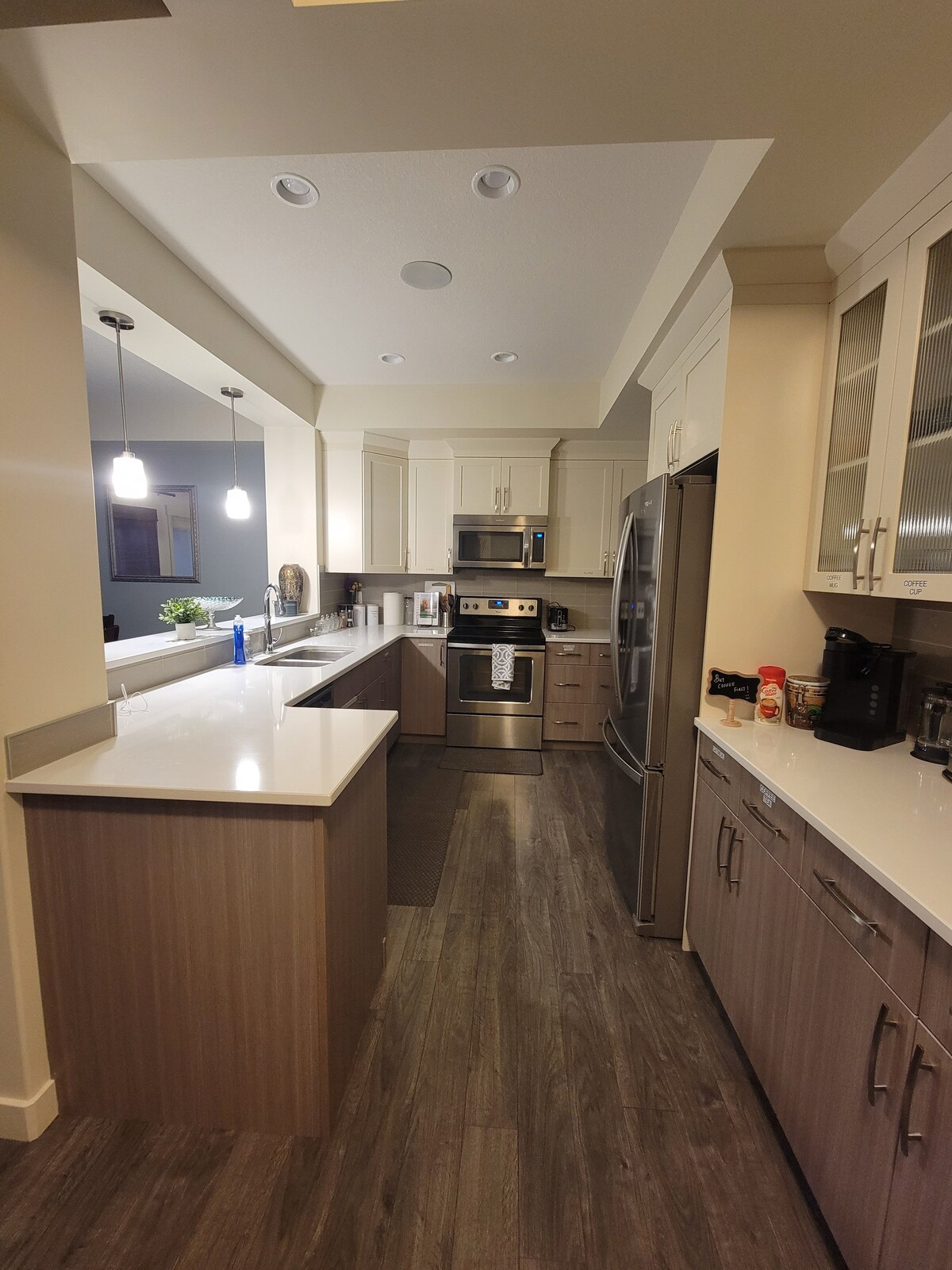 A modern kitchen is presented, featuring sleek cabinetry and stainless steel appliances. The spacious counter, with bar seating, is complemented by under-cabinet lighting. A large pantry is visible, alongside a coffee machine and other essential kitchen items, showcasing an inviting area for meal preparation.