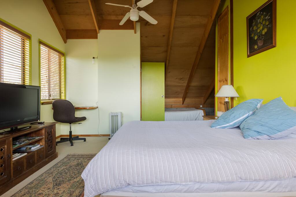 Main bedroom with ensuite, TV, desk, queen bed and single bed in background.