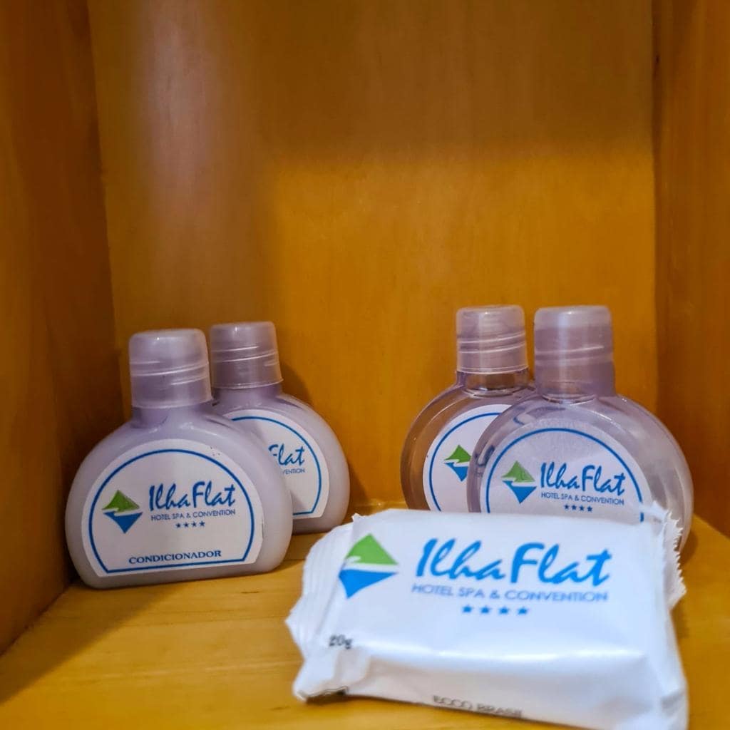 Toiletries are displayed on a wooden shelf, including four bottles of conditioner and a wrapped soap bar. Each item is branded with the hotel logo, indicating a focus on guest comfort and convenience.