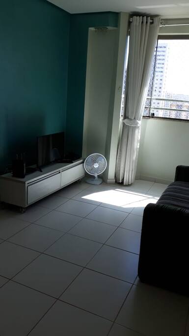 Sala com sofá cama, mesa, rack, TV, cortinas