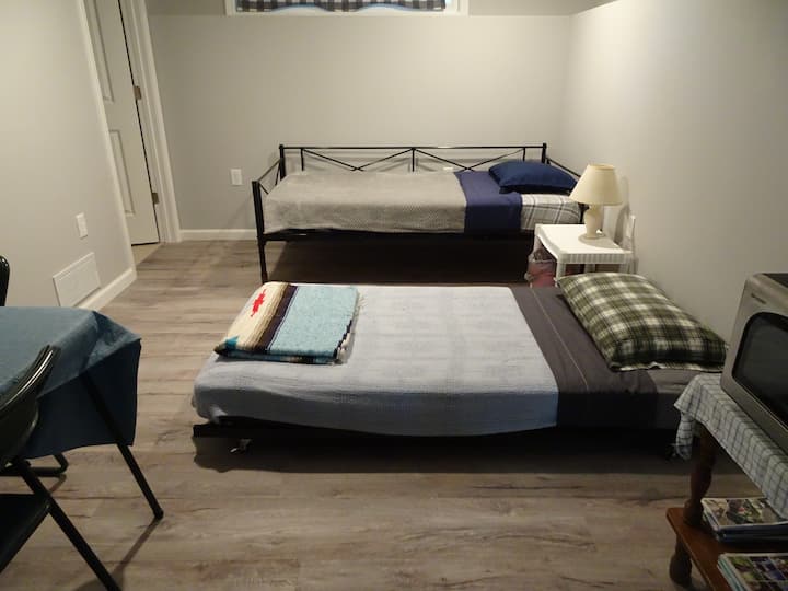 basement bedroom with 2 twin beds (the shorter one rolls under the taller one), microwave-toaster oven, & card table with 2 chairs