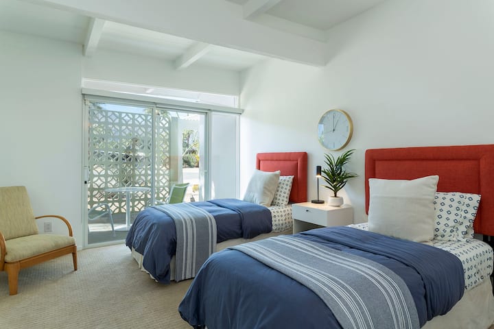 בחדר השינה הזה עם שתי מיטות יחיד יש פטיו פרטי משלו עם שולחן וכיסאות.