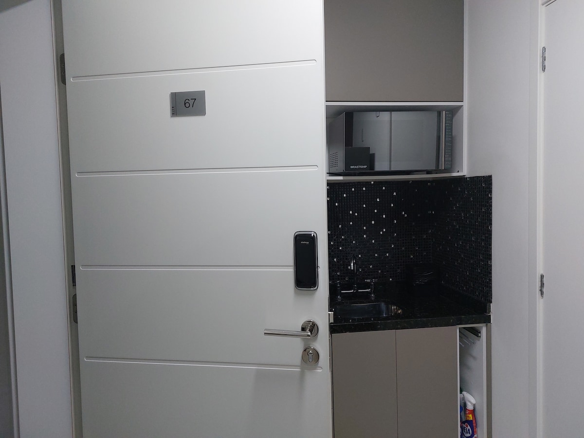 A well-maintained entrance door labeled with the number 67 opens into a compact kitchenette area. The kitchenette includes a black granite countertop, microwave, and a small sink. The modern design is complemented by the sleek cabinetry, ensuring a functional space.