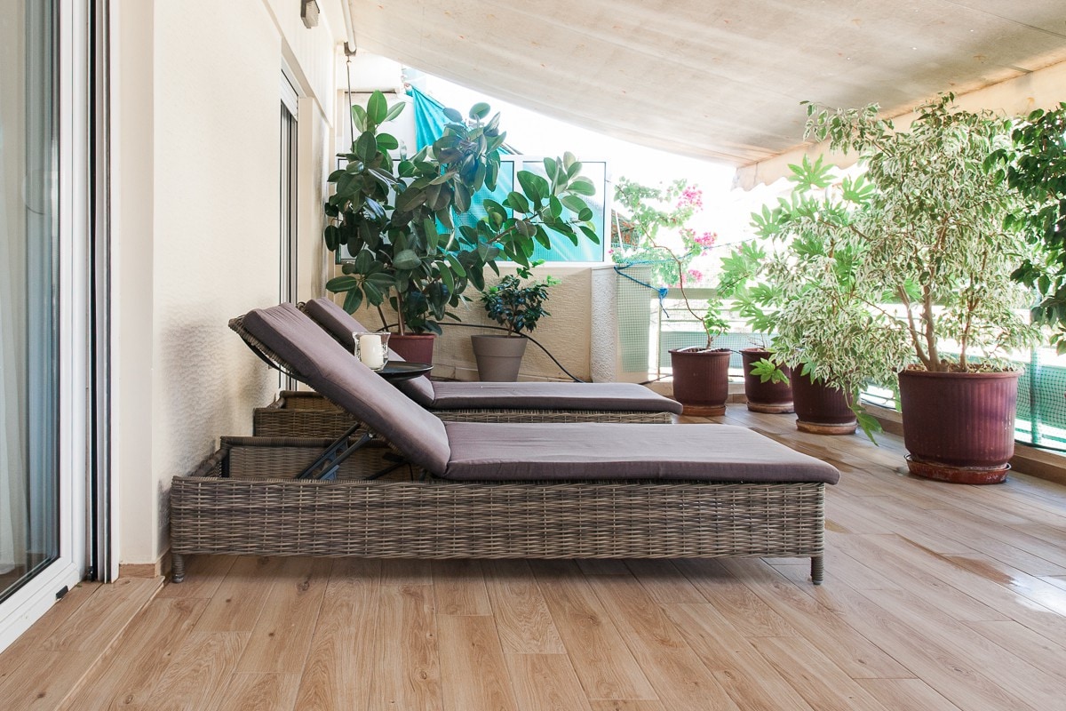 Two comfortable loungers are positioned on the spacious balcony, surrounded by lush potted plants. The flooring features a natural wood design, complementing the relaxing outdoor space that provides a tranquil setting for leisure and enjoyment.