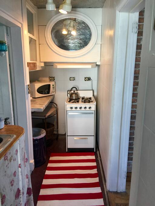 Kitchen with stove, refrigerator, microwave, coffee maker, tea kettle, cookware, plates, bowls, glasses, silverware, etc.